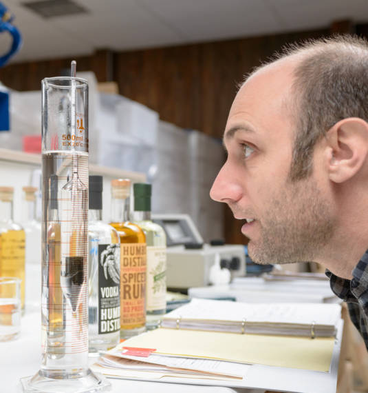 Distiller examining beaker of liquid