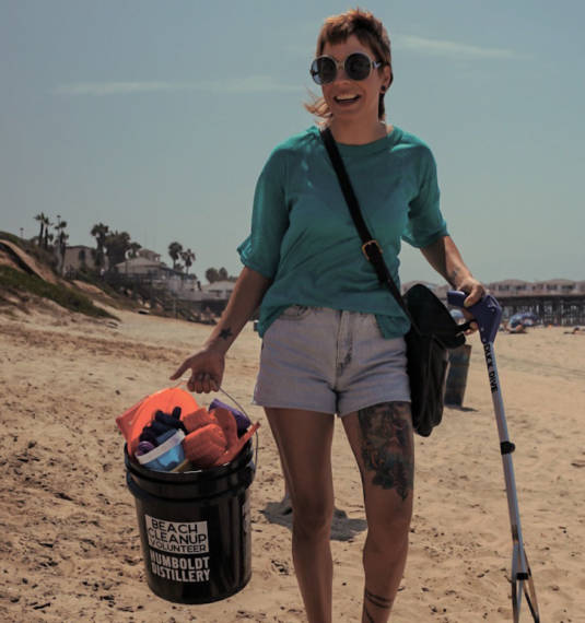 A person stands on a beach, holding a bucket labelled 